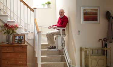 Ikääntynyt mies laskeutuu iloisena portaita Stannah-porrashissillä.