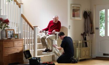 Vanhempi mies istui iloisena Stannah-porrashississään, kun Stannahin pätevä teknikko viimeisteli sen asennusta.